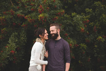 a happy couple standing in front of a bush with red berries 