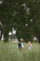 a couple holding hands and walking through a field 