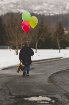 boy child walking outdoors in the snow carrying a teddy bear and balloons 