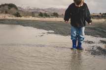 boy child in rain boots splashing in a puddle
