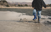 boy child in rain boots splashing in a puddle 