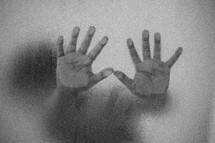 child's hands pressed against wet glass 