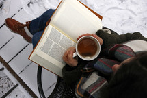 a woman reading a Bible outdoors in winter snow and has a tea cup 
