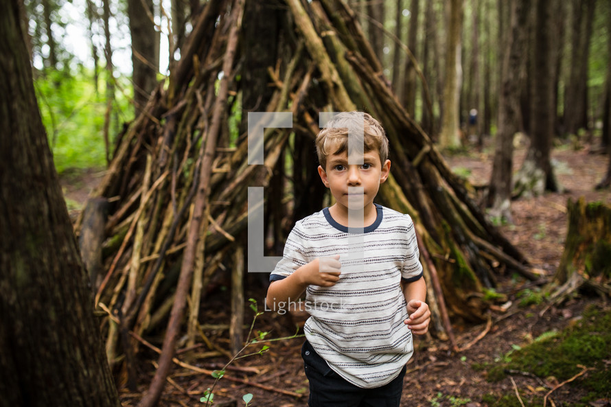 boy and a teepee of sticks in the woods 