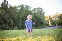 A little boy running through a field of green grass.