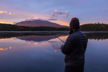 a man fishing on a lake shore at sunrise 