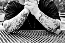 man with a tattoo of But the gift of God is eternal on his arm praying 