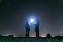Men in park at night shining flashlight