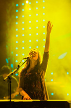 Woman with raised hand singing and playing keyboard worship leader praise