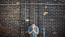 Man praying in front of brick wall