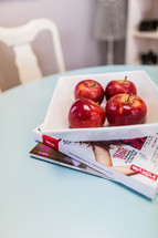 Bowl of red apples on table with magazines