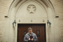 man holding a bible in front of church doors