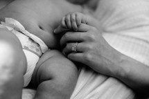 Woman's hand holding infant's hand while lying side by side.