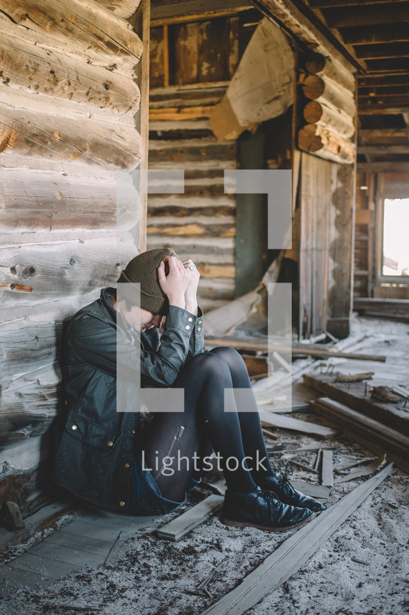 A girl sits with head in hands in an abandoned log house.