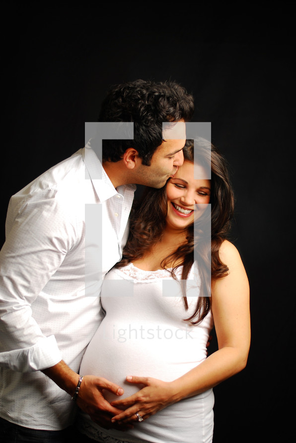 man kissing a pregnant woman on the forehead