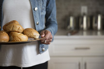 a woman holding a tray of bread buns 