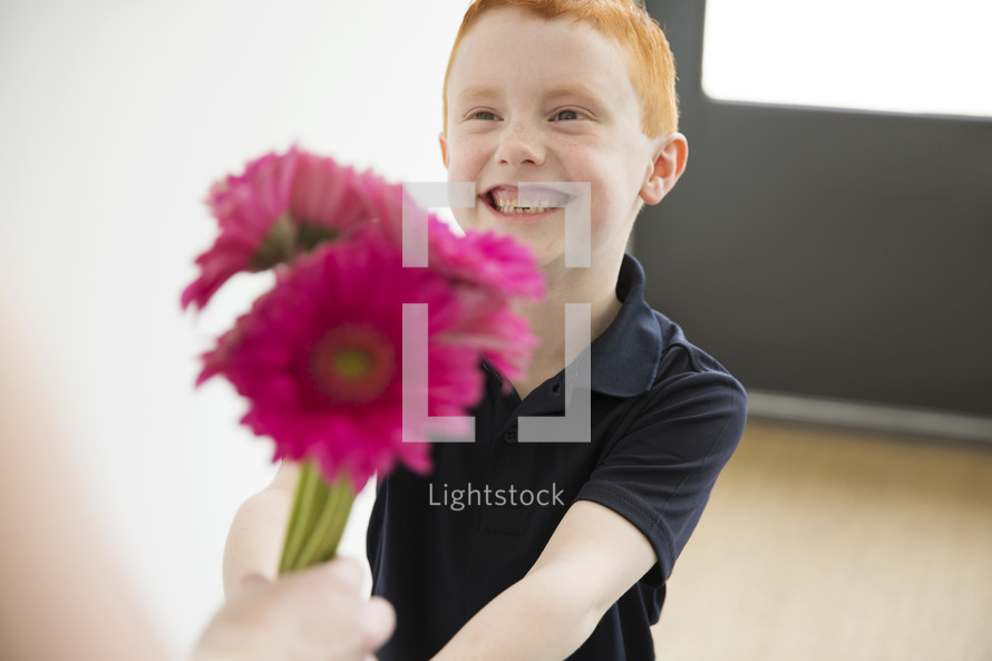 A smiling boy giving a bouquet of pink flowers.