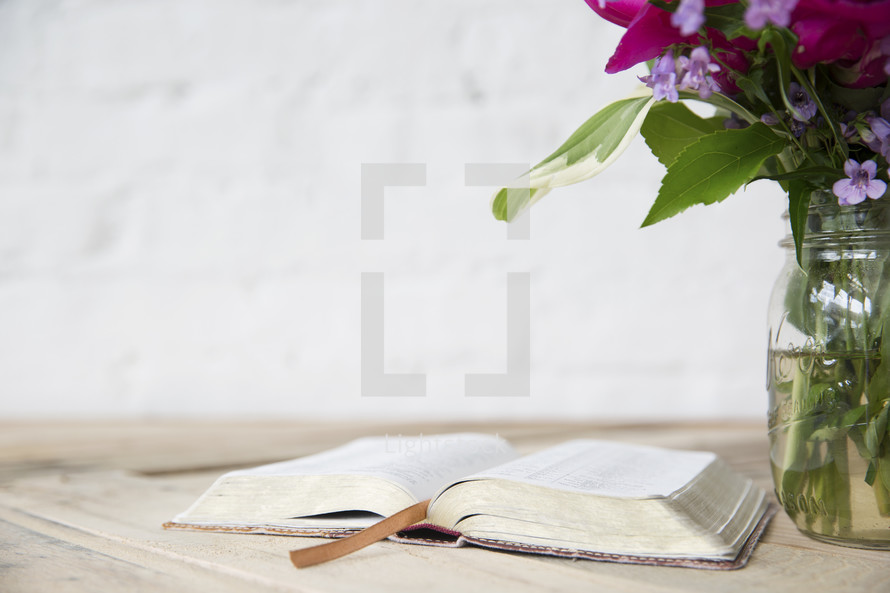 open Bible, and flowers in a vase on a wood table 