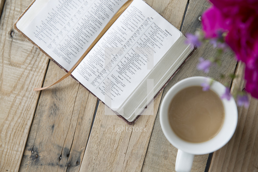 coffee mug, open Bible, and flowers in a vase on a wood table 