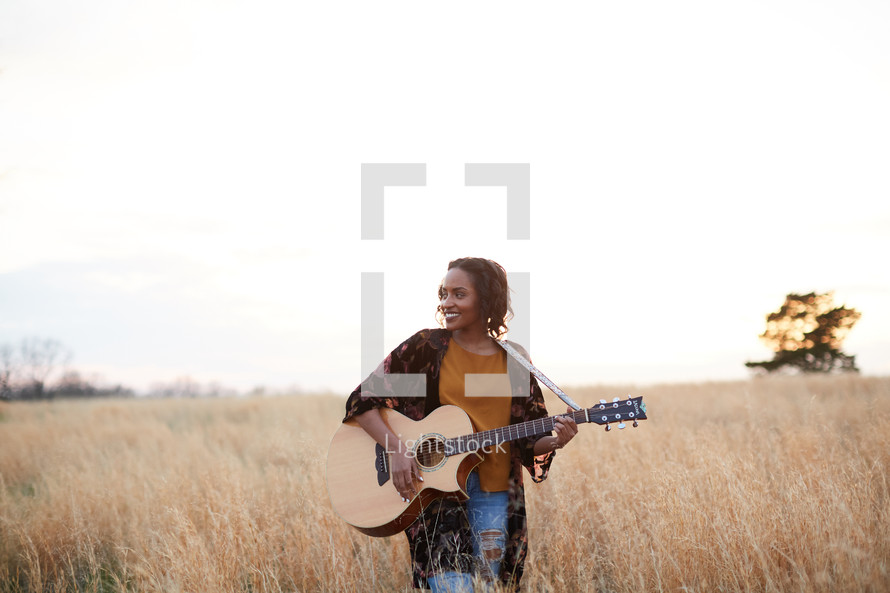 a woman standing in a field with a guitar 
