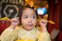 silly Asian child with fork and knife ready to eat in restaurant.