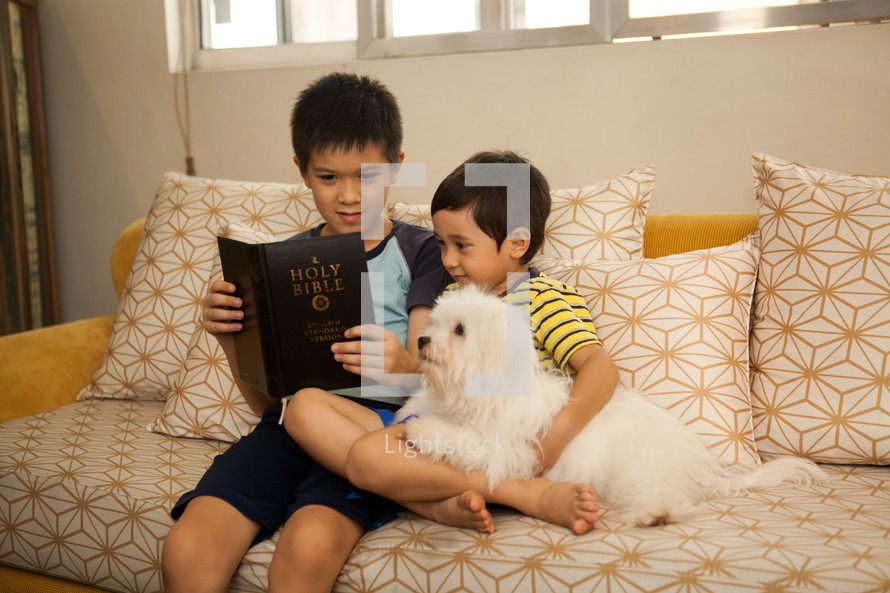 brothers sitting on a couch reading a Bible with their dog 
