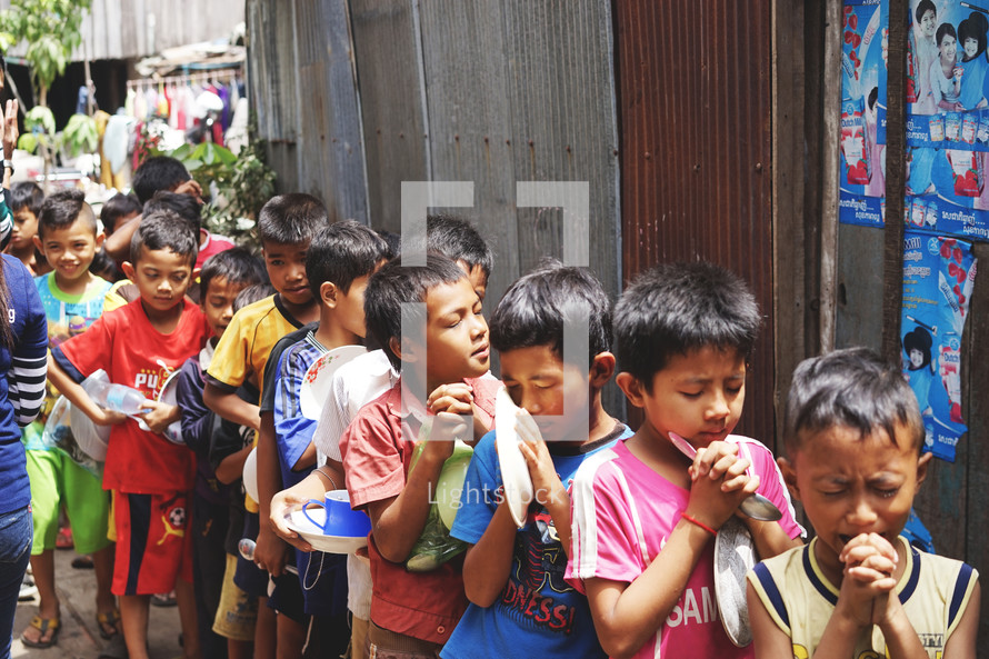 children in line holding bowls praying 