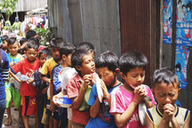 children in line holding bowls praying 