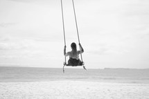 a woman on a rope swing on a beach 