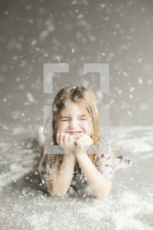 Joyful little girl in studio with snow falling on grey background