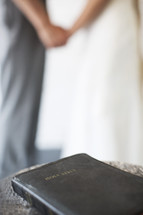 bride and groom holding hands with a Bible in the foreground.