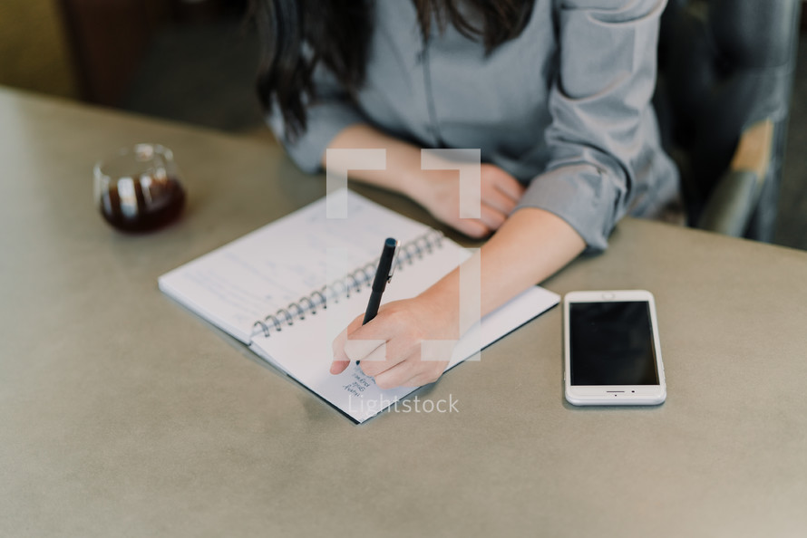 a businesswoman sitting at a desk writing notes in a planner 