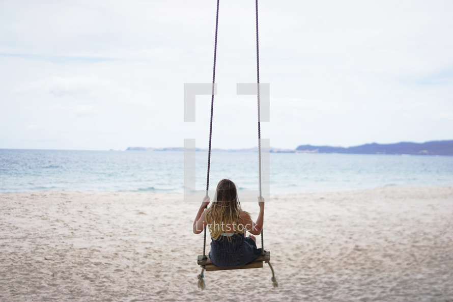 a woman on a rope swing on a beach 
