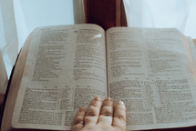hand on the pages of a Bible in a window 