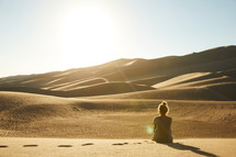 a woman sitting in a desert looking out at the view 