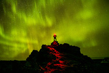 A man standing at the top of a mountain under the glow of star light.