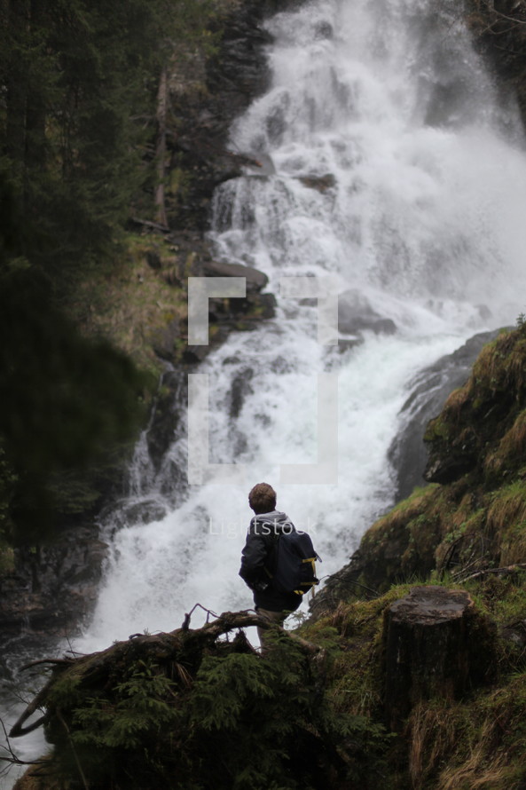 man hiking up a mountain near a waterfall 