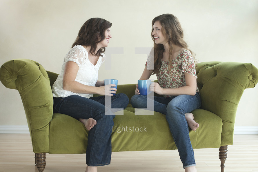 two friends drinking coffee and talking on a couch