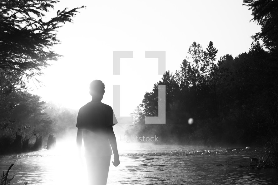 a young man standing by a river under intense sunlight 