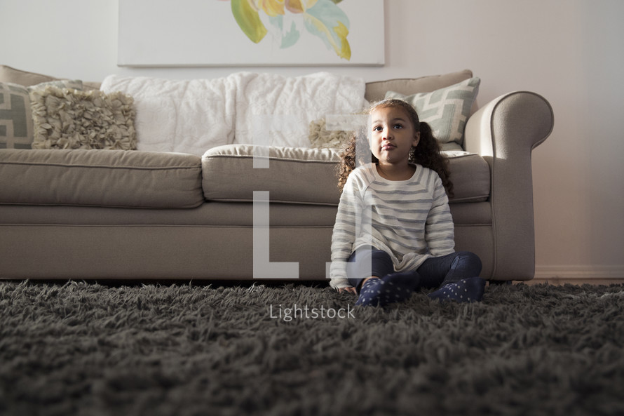 a girl child sitting on a rug in a living room 