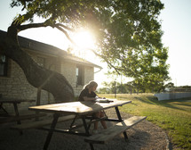 teen girl sitting at a picnic table reading a Bible 