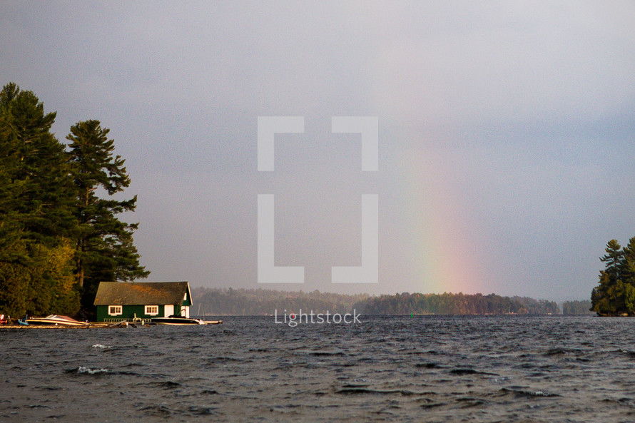 A beautiful rainbow shelters a house by a lake on an autumn day.
