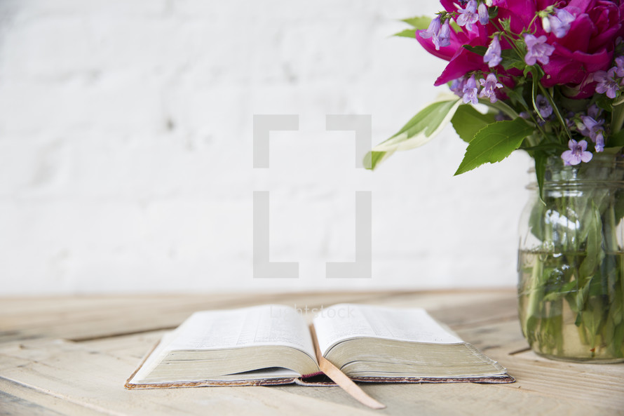 open Bible and flower in a vase on a table 