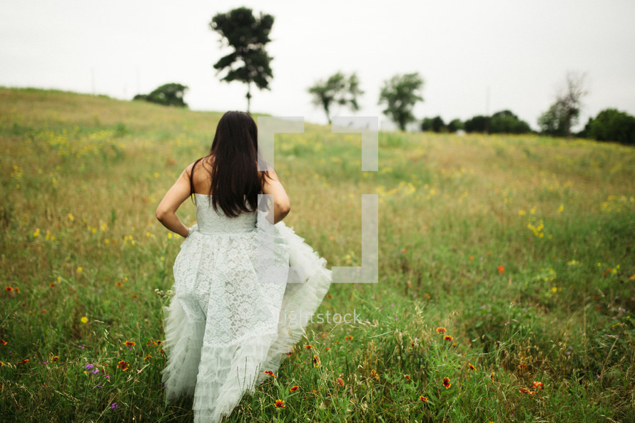 woman in a white dress walking through a meadow of wildflowers 