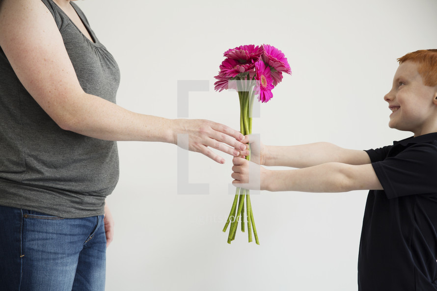 A little boy gives his mother a bouquet of pink flowers.