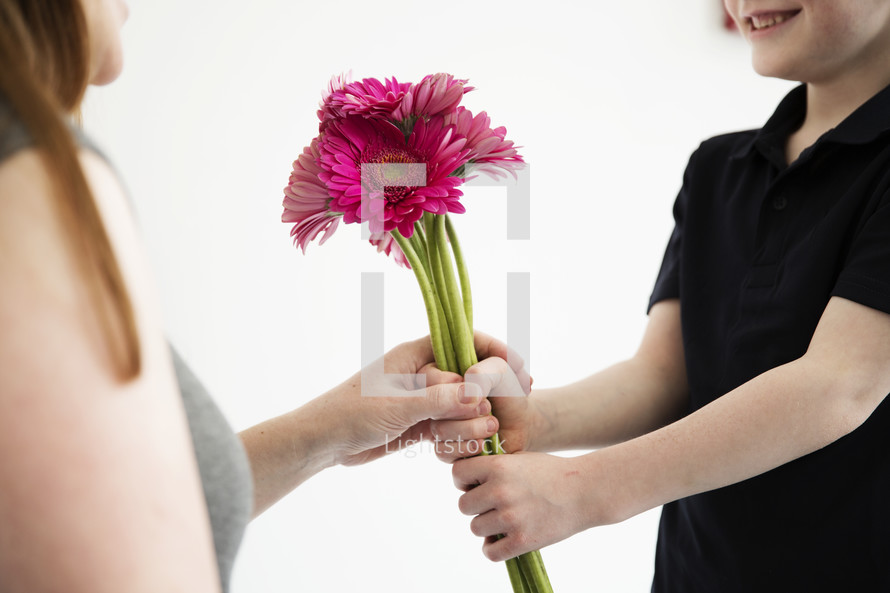 A boy gives his mother a bouquet of pink flowers.