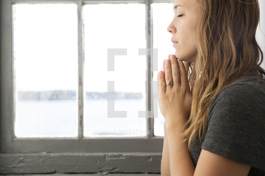 a young woman in prayer by a window 