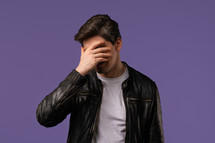 Worried man doing facepalm gesture, covering face with hands, like no, I forgot. Disappointed guy feeling sorrow, regret, drama, failure, problems on violet background. High quality