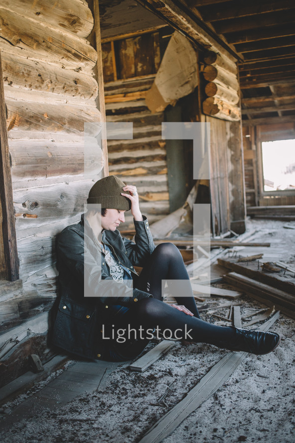 A woman sitting with hand on head in an abandoned log house.