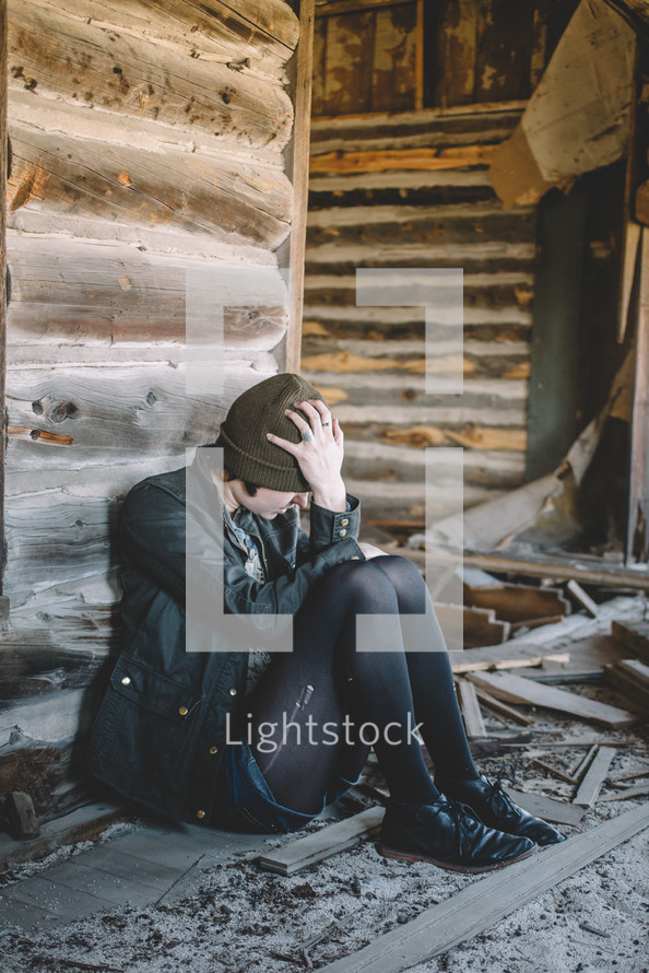 A woman sitting with head in hands in an abandoned log house.